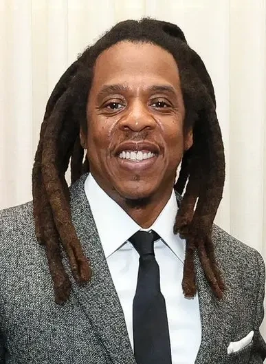 Jay-Z smiling in a suit and tie at an official event
